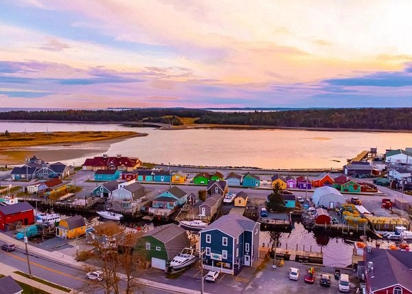 Aerial view of Fisherman’s Cove in Eastern Passage, Nova Scotia, showing colourful waterfront buildings, boats, and calm harbour water at sunset