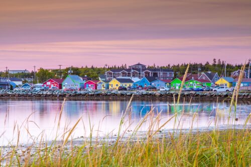 Row of brightly coloured houses along the waterfront in Eastern Passage, Nova Scotia, reflected in calm harbour water at sunset