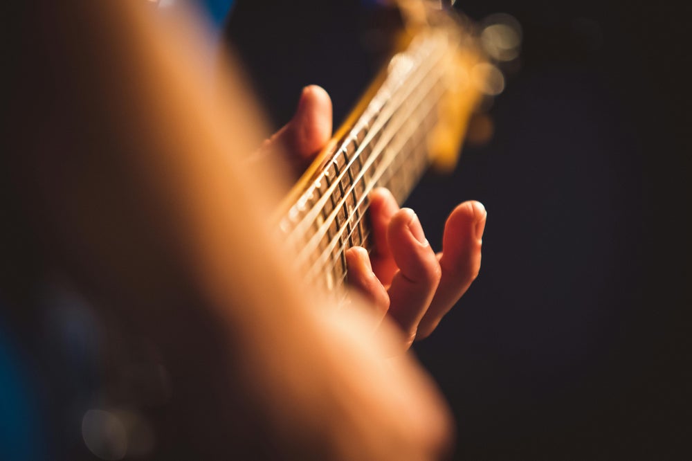 Close-up of hands playing an electric guitar on stage with warm lighting and bokeh background.
