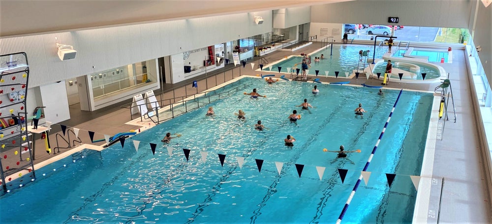 East Hants Aquatic Centre Indoor Pool People participating in a group swim class in the indoor pool at the East Hants Aquatic Centre, with lanes, shallow area, and bright open space