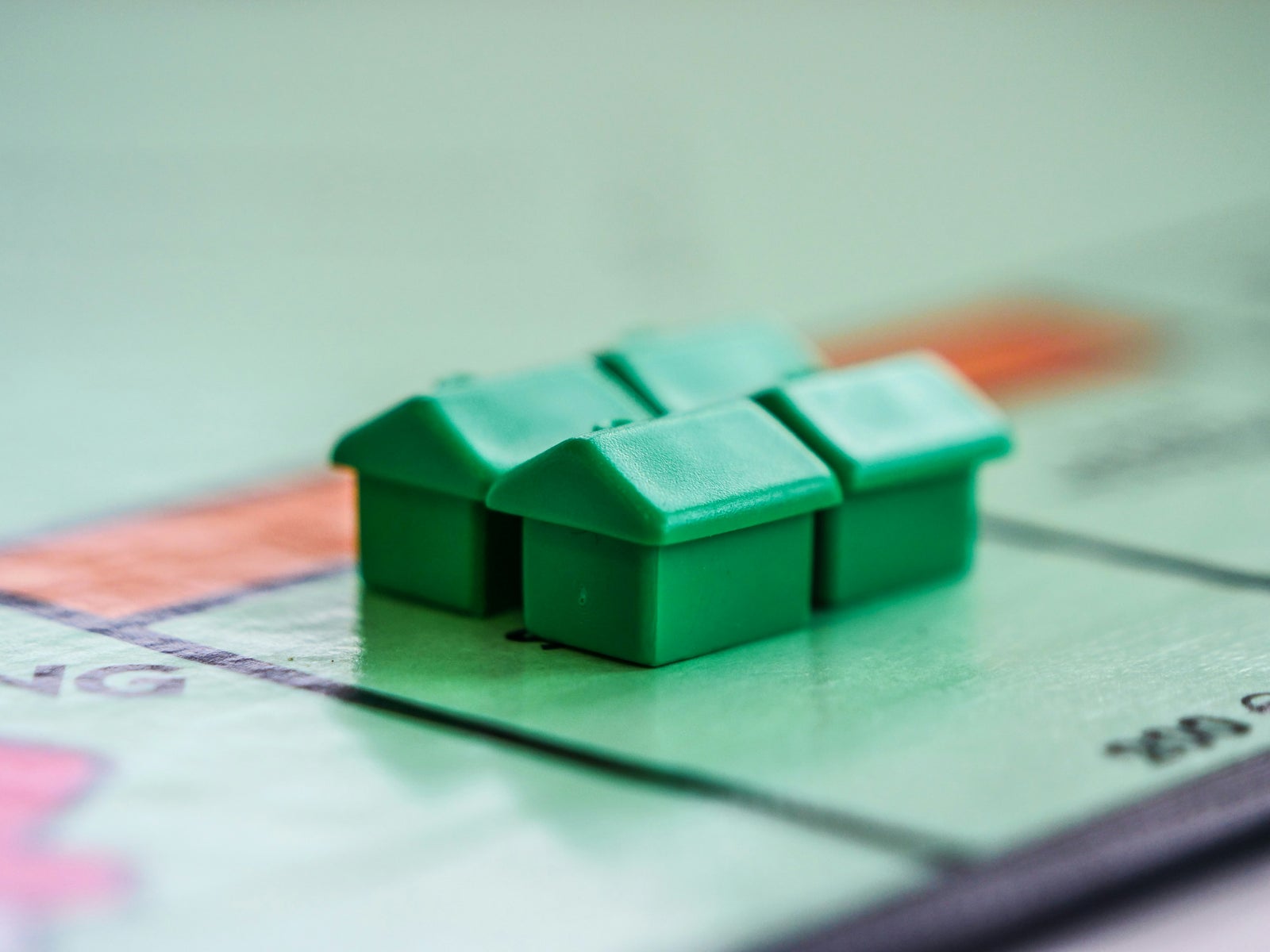 Green Monopoly houses representing real estate decisions when choosing to buy first or sell first.