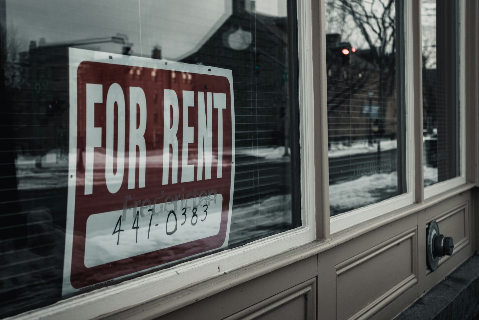 For rent sign displayed in a storefront window, representing the ongoing cost of renting a home.
