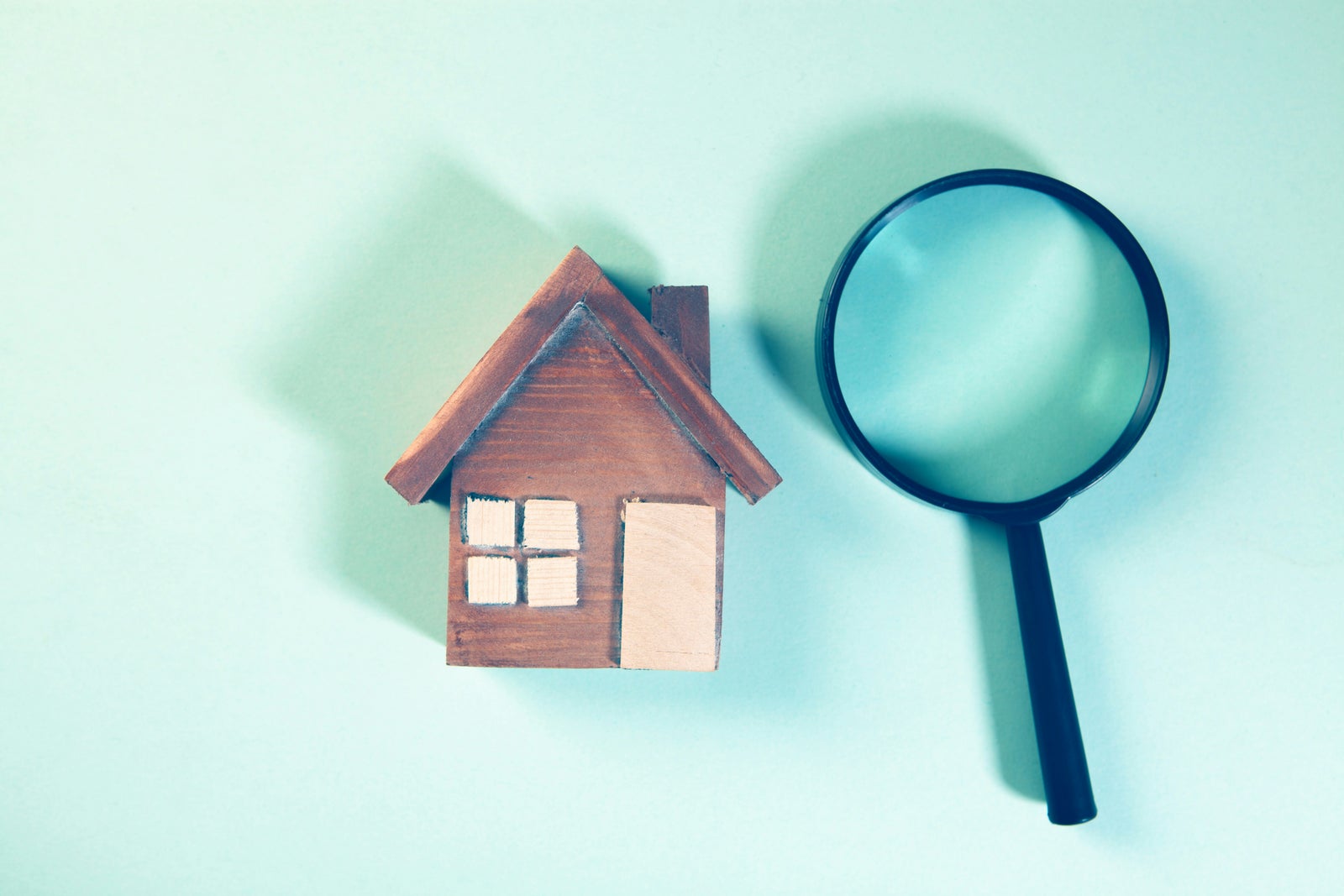 Model home and magnifying glass symbolizing a professional home inspection before purchasing a property.