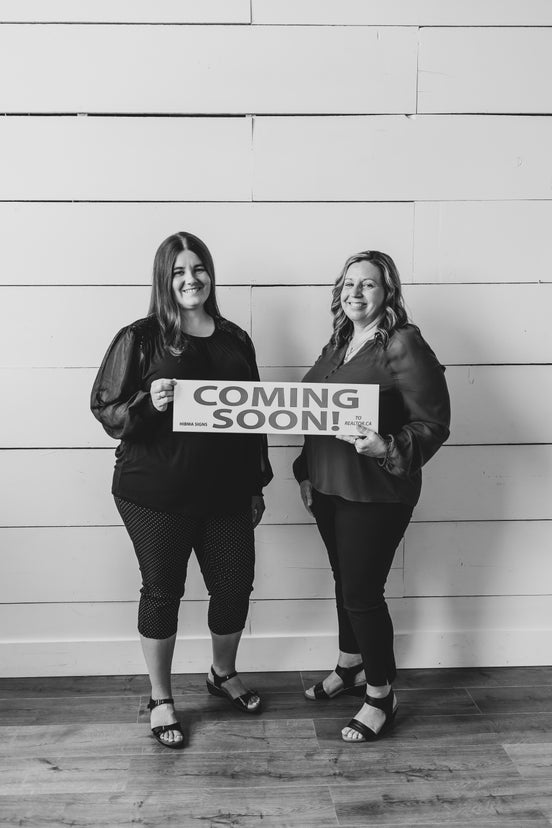 Sheri and Cassidy hold a coming soon sign
