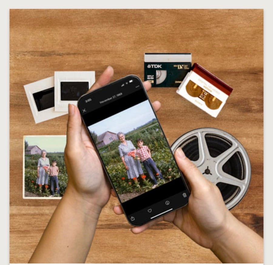 Hands holding a smartphone displaying a family photo, surrounded by printed photos, slides and a film reel.