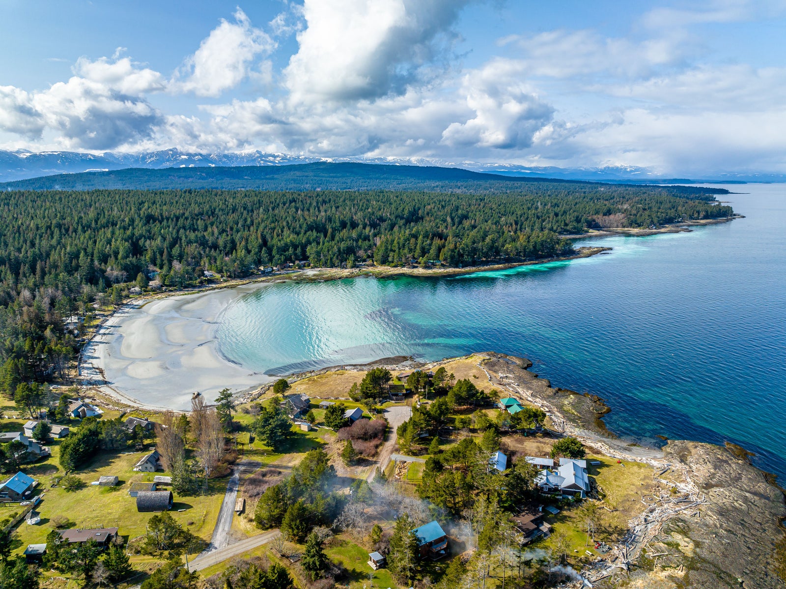Aerial view of a coastal Vancouver Island community with homes, forest, beach, ocean and mountain views