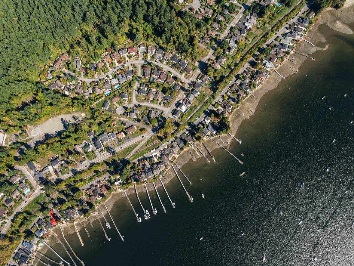 Aerial view of waterfront homes in Port Moody, surrounded by lush forests and docks extending into the water, highlighting exclusive real estate opportunities