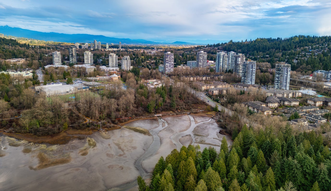 Aerial view of Port Moody's residential buildings surrounded by lush forests and waterfront, showcasing prime real estate opportunities in a scenic environment