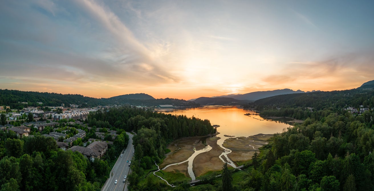 Aerial view of Port Moody Centre at sunset, showcasing the beautiful Burrard Inlet and lush green surroundings, highlighting the prime real estate market in Port Moody Centre