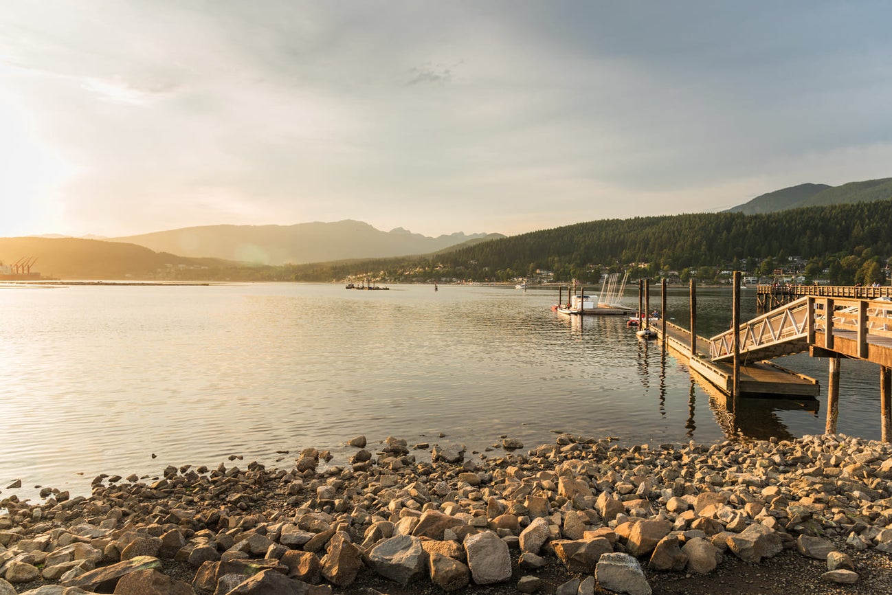 Serene waterfront view in Port Moody at sunset, with a dock and surrounding mountains, highlighting peaceful real estate opportunities in the area.