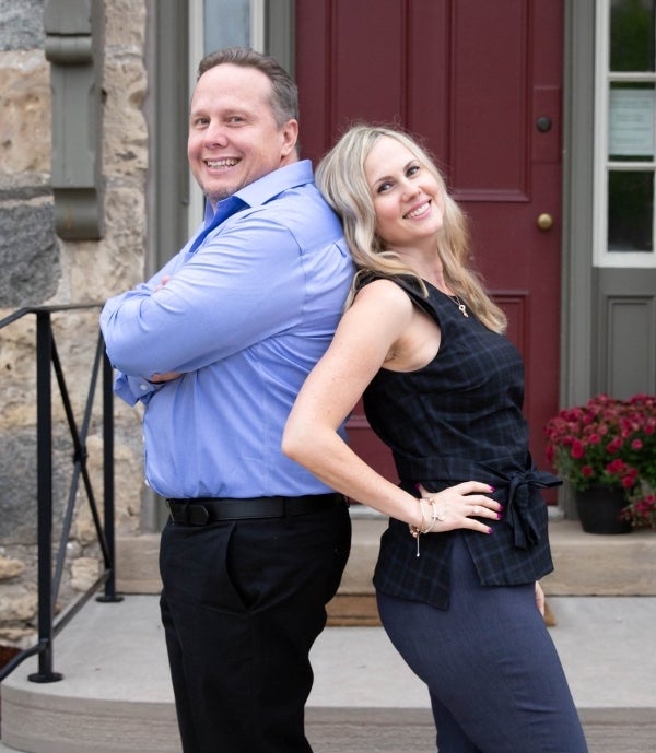 Photo of Marcia & Ryan Grove, REALTORS® smiling and standing back to back.