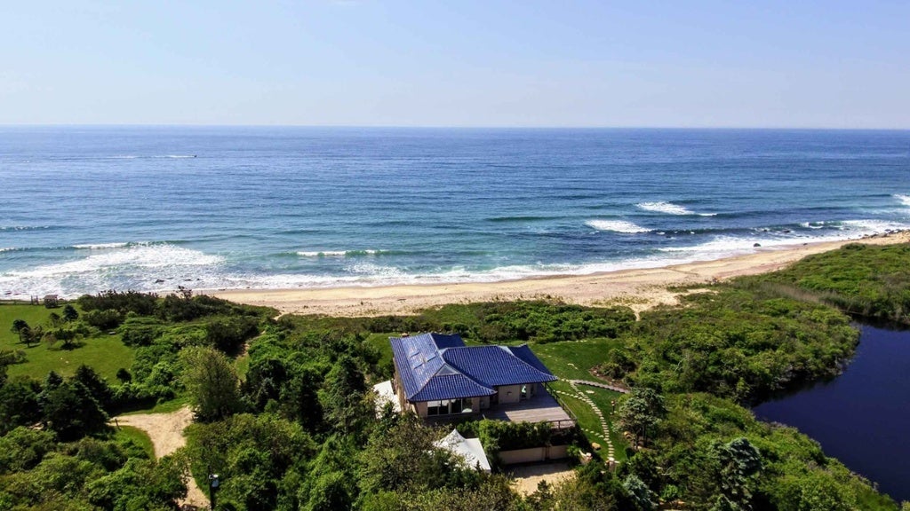 This extraordinary property is an oceanfront masterpiece on 36 private and verdant acres in exclusive Montauk Point, the Malibu of the East Coast. The 7,000-square-foot main house is the vision of architect Frank Hollenbeck, who based the design on a Chinese tea house, evidenced in the beautiful pagoda-style blue-tiled roof. It is ideally situated on a high bluff overlooking the Atlantic Ocean and a secluded, sandy beach with no public access for miles. The property includes a two-acre pond which provides habitat for local flora and fauna. At the ocean’s edge, two naturally formed 100-foot jetties act as barriers to passing storms.