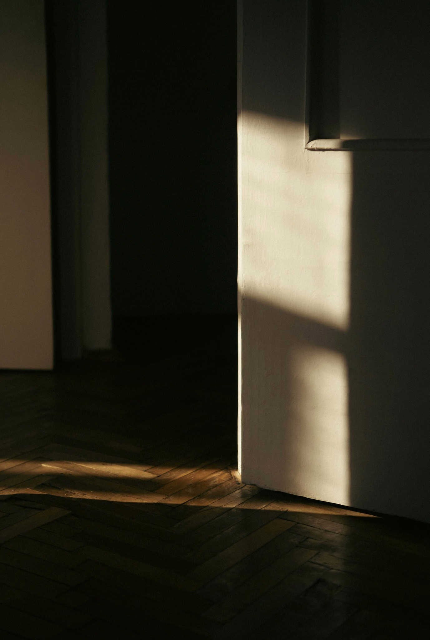 Sunlight crossing an interior wall and parquet floor.