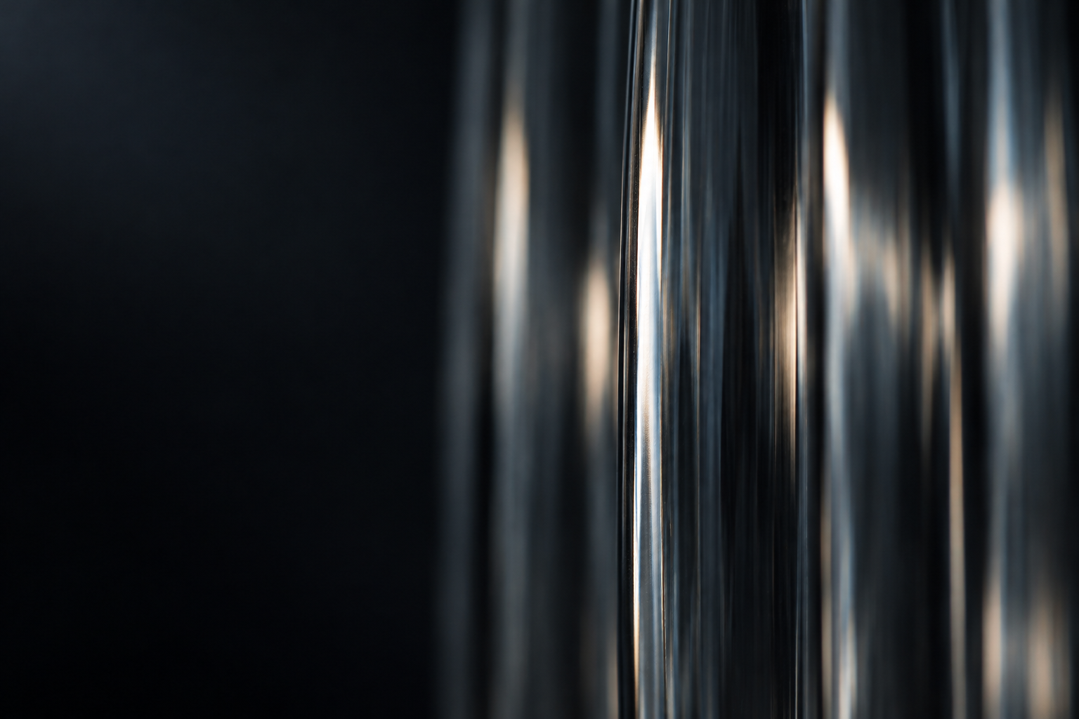 A single silver-lit ridge of fluted glass, with the adjacent ribs receding into shadow.