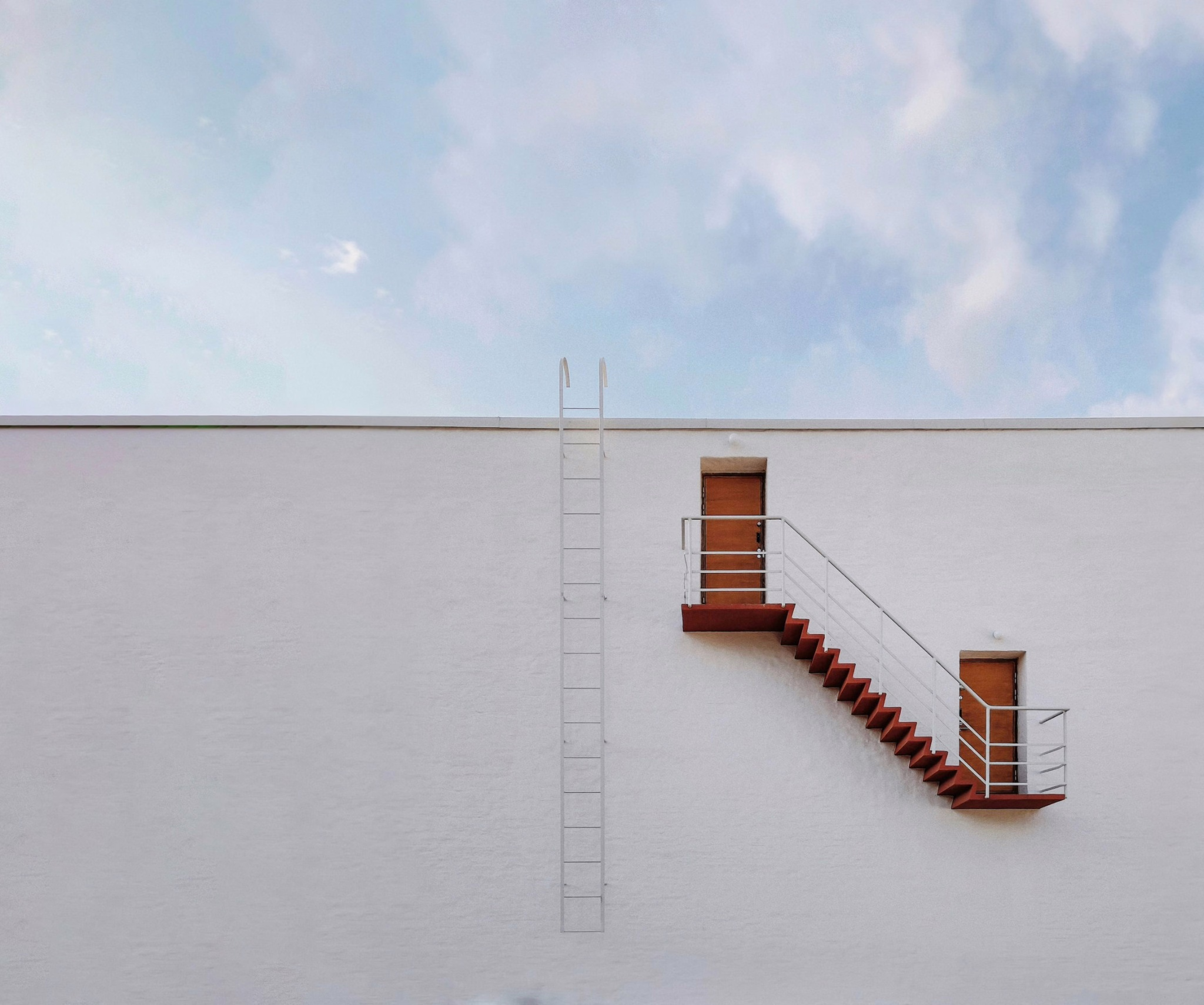 Exterior stairs connecting two doors against a pale wall.