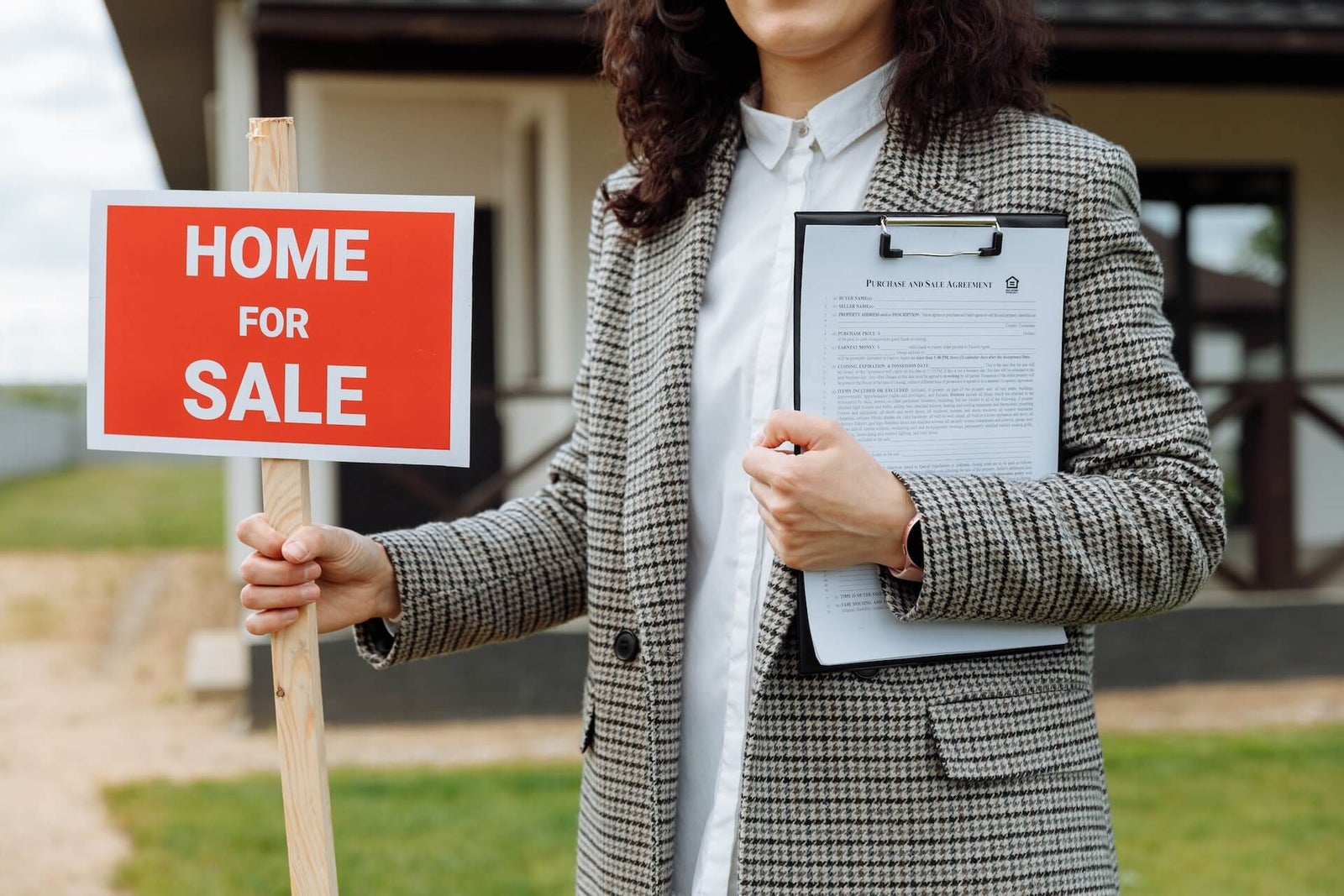 Woman wearing a blazer and holding a red home for sale sign