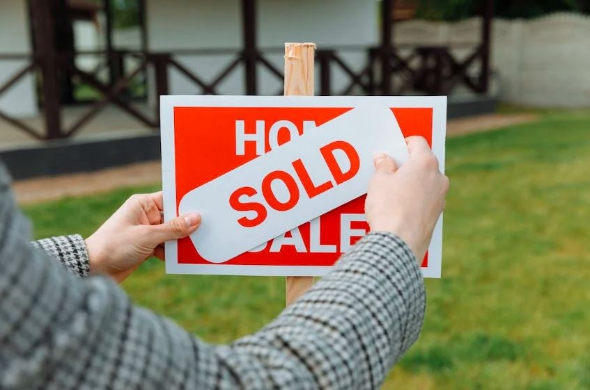 real estate agent placing “sold” sign over “house for sale” sign