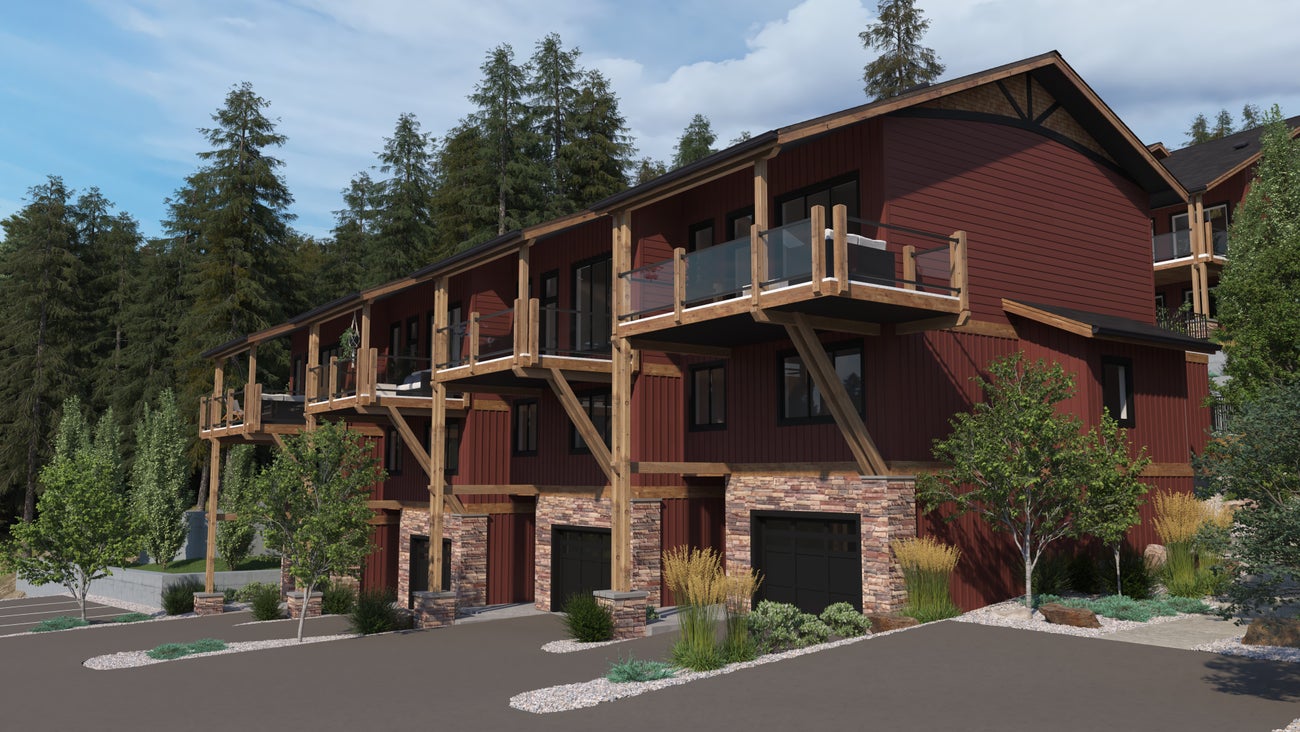 Architectural view of Fairmont townhomes showcasing multiple units with red and natural wood siding, expansive balconies, and stone accents, set against a backdrop of evergreen trees under a clear sky