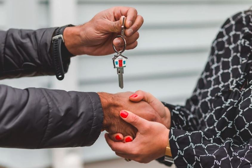 buyer’s realtor and buyer shaking hands while exchanging house key]