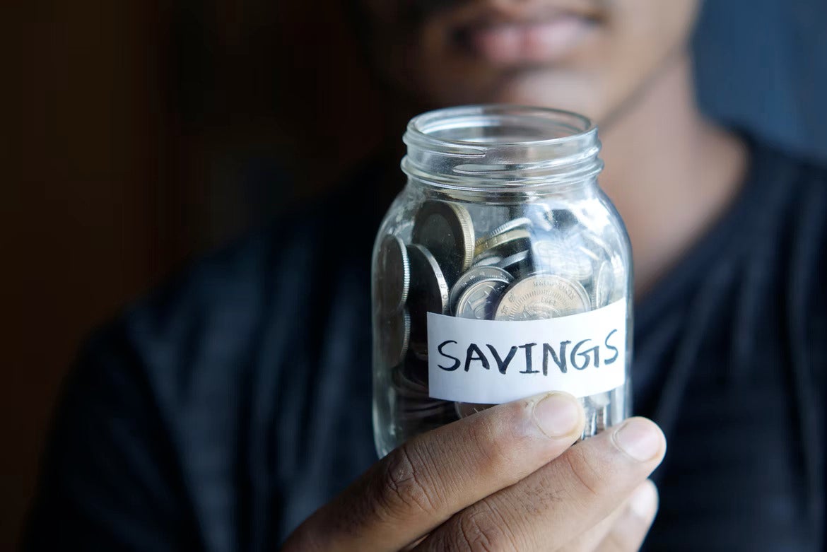 person holding a jar full of coins with “savings” label