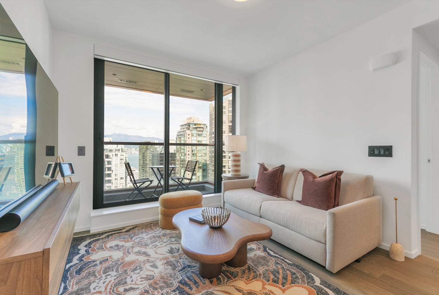 Modern furnished rental in downtown Vancouver featuring a bright living room with sofa, coffee table, and city views from large windows.