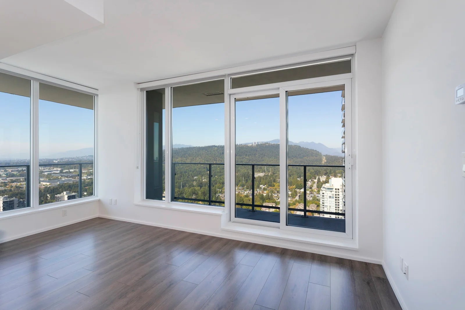 Empty highrise condo living room in Metro Vancouver with floor-to-ceiling windows and mountain views